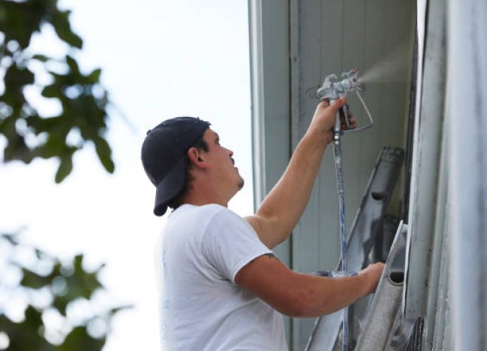 Man Spraying Paint On Exterior of Old Home